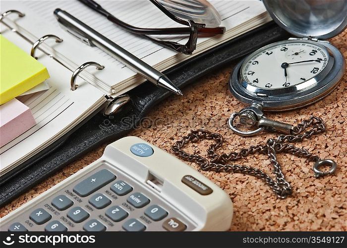 pocket watch and notebook on a cork board