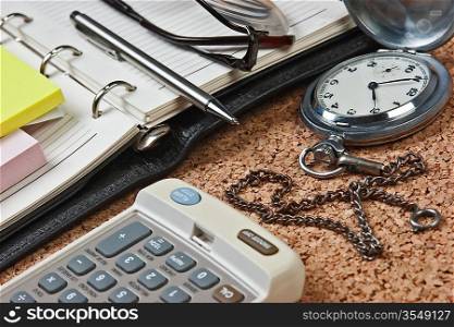 pocket watch and notebook on a cork board