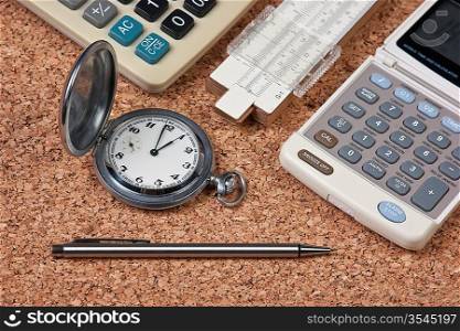 pocket watch, calculator and slide rule on a cork board