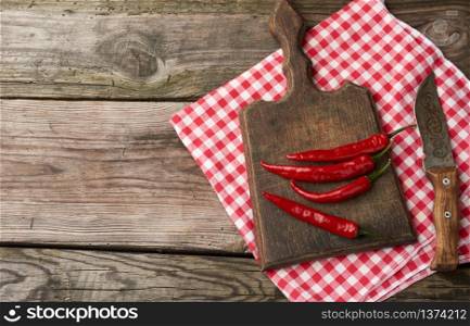 pods of red chili peppers on a brown cutting wooden board, gray table, top view, copy space