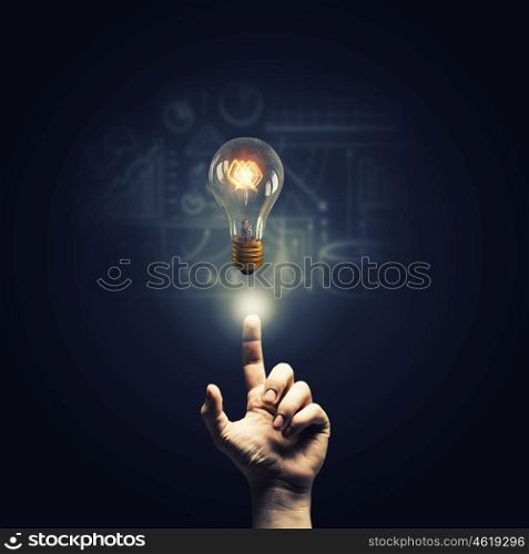 Pointing idea. Close up of human hand pointing with finger on glass glowing light bulb