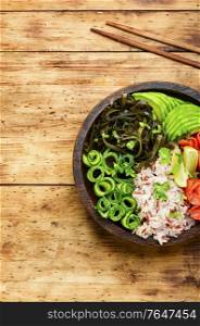 Poke bowl with salmon and vegetables on wooden table. Hawaiian salmon fish poke bowl