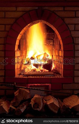 poker, firewood and flames of fire in fireplace in evening time