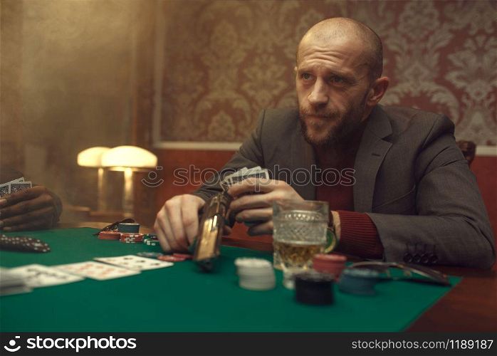 Poker player with gun plays in casino, risk. Games of chance addiction. Man leisures in gambling house, gaming table with green cloth