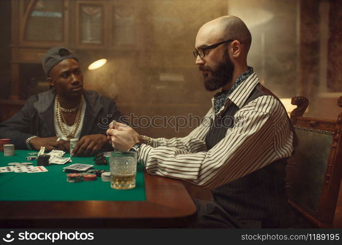 Poker players place money bets on gaming table with green cloth in casino. Games of chance addiction, risk, gambling house. Men leisures with whiskey and cigars. Poker players place money bets on gaming table