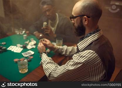 Poker players place money bets on gaming table with green cloth in casino. Games of chance addiction, risk, gambling house. Men leisures with whiskey and cigars