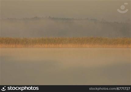 Poland.Bory Tucholskie National Park in August.Morning fog on the lake, overexposed light of the rising sun.Horizontal view.