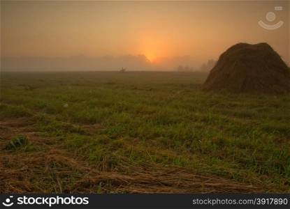 Poland,late summer.Dawn above meadows in the vicinity of the Narew river.On the foreground the one can see the mound of the cut grass and in the background of the fog and the glow of the rising sun.Horizontal view.