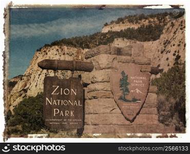 Polaroid transfer of wooden and stone sign for Zion National Park, Utah with rocky cliffs in the background.