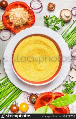 Polenta dish and various vegetables and seasoning ingredients for tasty vegetarian cooking on light rustic wooden background, top view composing, close up. Healthy eating and diet food concept.
