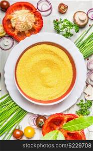 Polenta dish and various vegetables and seasoning ingredients for tasty vegetarian cooking on light rustic wooden background, top view composing, close up. Healthy eating and diet food concept.