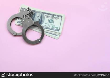 Police handcuffs and hundreds of us dollars lie on a background of living coral color. The concept of punishment for breaking the law in financial transactions. Police handcuffs and hundreds of us dollars lie on a pink background