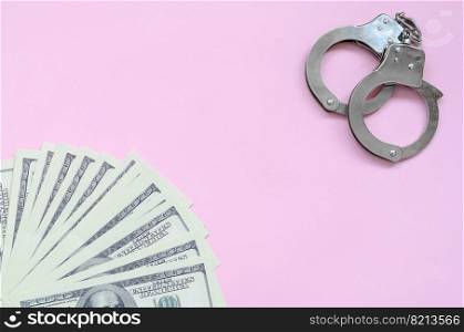 Police handcuffs and hundreds of us dollars lie on a background of living coral color. The concept of punishment for breaking the law in financial transactions. Police handcuffs and hundreds of us dollars lie on a pink background