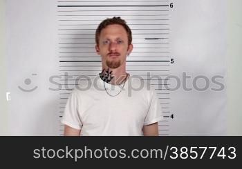 Police mug shots of a male criminal holding a placard, standing in front of a white rulered wall.