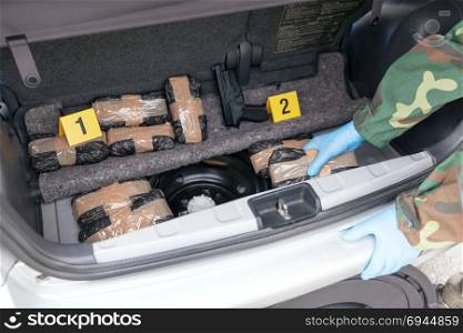 Police officer holding drug package found in the trunk of a car