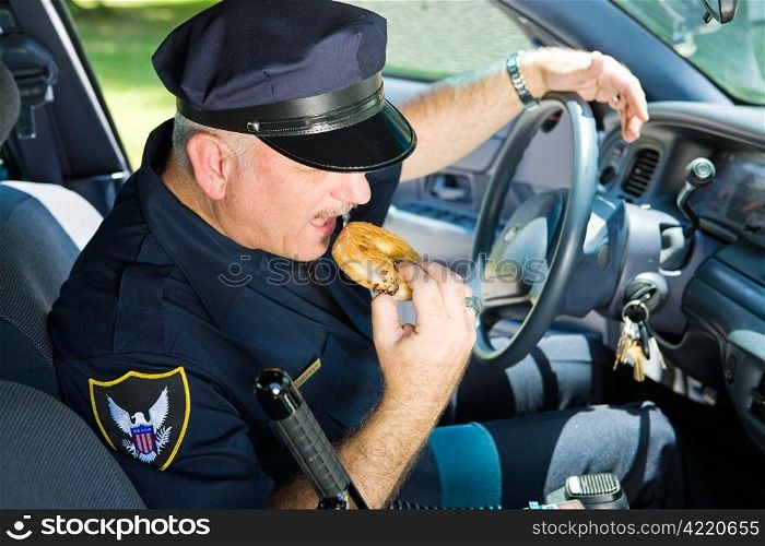 Police officer in his squad car, taking a bit from a donut.