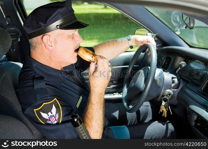 Police officer snacking on a donut while sitting in his squad car.