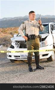 Police officer using radio in front of damaged car in desert