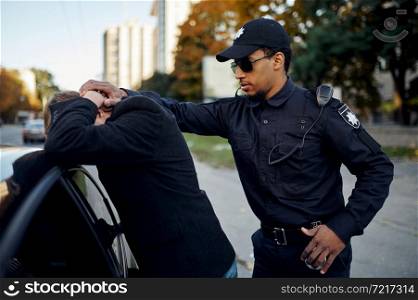 Police patrol arrests male driver near the car. Policeman in uniform protect the law, registration of an offense. Cop works on city street, order and justice control. Police patrol arrests male driver near the car