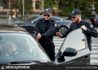 Police patrol with gun arrests female driver. Policemen in uniform protect the law, registration of an offense. Cops work on city street, order and justice control. Police patrol with gun arrests female driver
