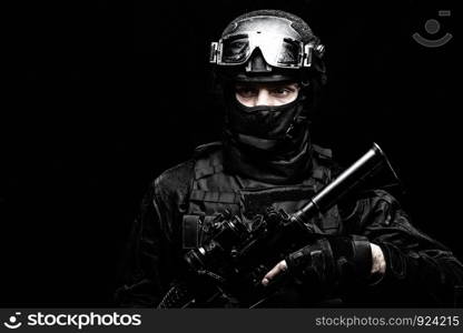 Police special operations fighter, SWAT shooter, secret service guard in black uniform, hidden behind mask identity, battle helmet with ballistic goggles, armed assault rifle, low key studio portrait. SWAT team fighter shoulder portrait on black