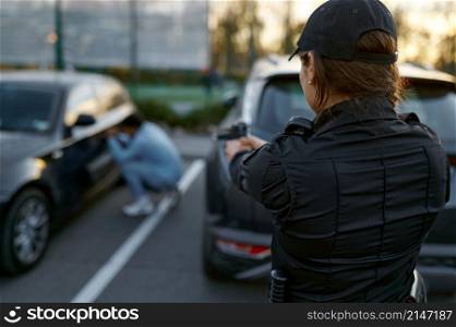 Policewoman aiming gun at car thief on blurred background. View from police officer back. Policewoman aiming gun at car thief backview