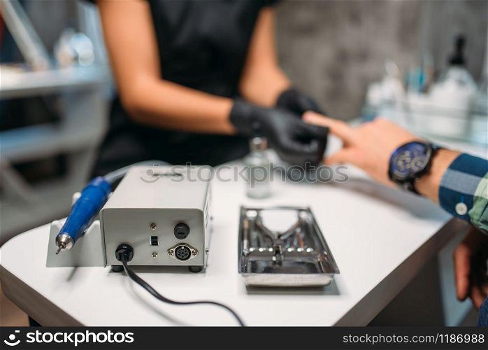 Polishing machine in nail salon, female beautician in black gloves makes a man manicure on background. Manicurist doing hand skin care procedure