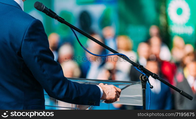 Political campaign. Unrecognizable politician on stage, speaking to the crowd during election campaign. Male Speaker Standing In Front Of Microphones