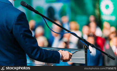 Political campaign. Unrecognizable politician on stage, speaking to the crowd during election campaign. Male Speaker Standing In Front Of Microphones