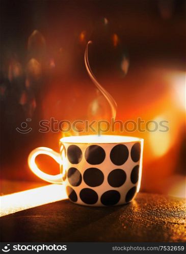 Polka dot cup with steam on table at orange color sunset light with bokeh. Indoor. Hot beverage