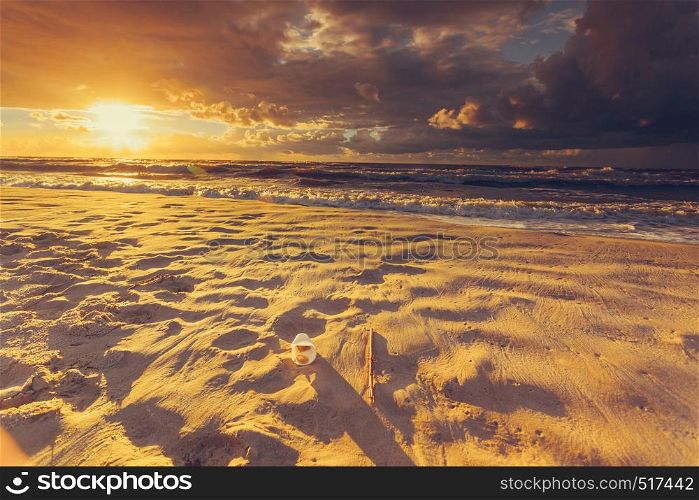 Polluted beach shore. Plastic disposable cup abandoned on sand, beautiful golden sunset in the background. Earth ecology. Plastic disposable cup on sea shore. Earth ecology