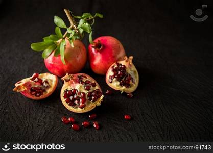 Pomegranate fruits and seeds over a textured black background. Pomegranate fruits and seeds