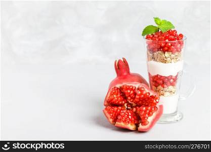 Pomegranate parfait - sweet organic layered dessert with granola flakes, yogurt and ripe fruit seeds in beautiful glasses on gray background with copy space. Natural vegetarian healthy food.. Pomegranate parfait - sweet organic layered dessert with granola flakes, yogurt and ripe fruit seeds.