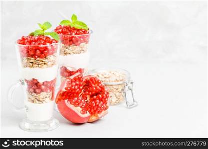 Pomegranate parfait - sweet organic layered dessert with granola flakes, yogurt and ripe fruit seeds in beautiful glasses on gray background with copy space. Natural vegetarian healthy food.. Pomegranate parfait - sweet organic layered dessert with granola flakes, yogurt and ripe fruit seeds.