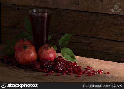 Pomegranate with juice in glass and pile of seeds on the wooden board on a dark background in dim light / still Life foods