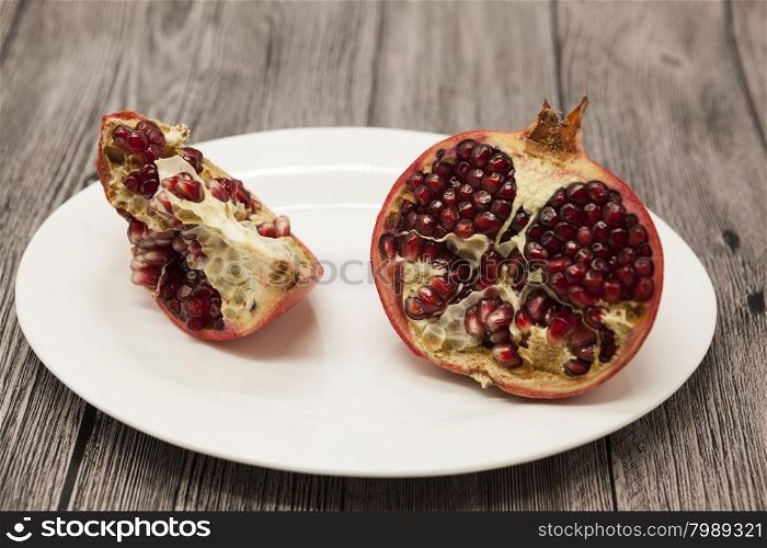 Pomegranates have broken into pieces with red berries on a porcelain plate on a dark background.. Pomegranates have broken into pieces with red berries on a porcelain plate on a dark background