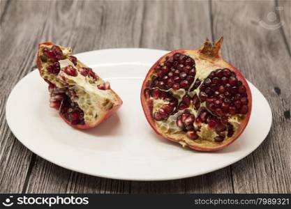 Pomegranates have broken into pieces with red berries on a porcelain plate on a dark background.. Pomegranates have broken into pieces with red berries on a porcelain plate on a dark background