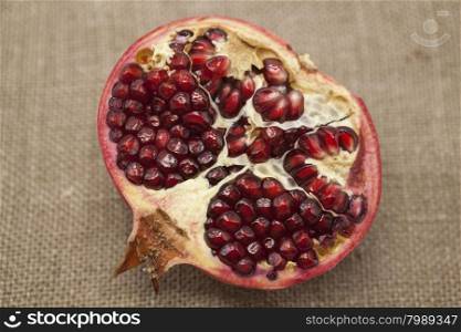 Pomegranates have broken into pieces with red berries on a porcelain plate on a textile background.. Pomegranates have broken into pieces with red berries on a porcelain plate on a textile background