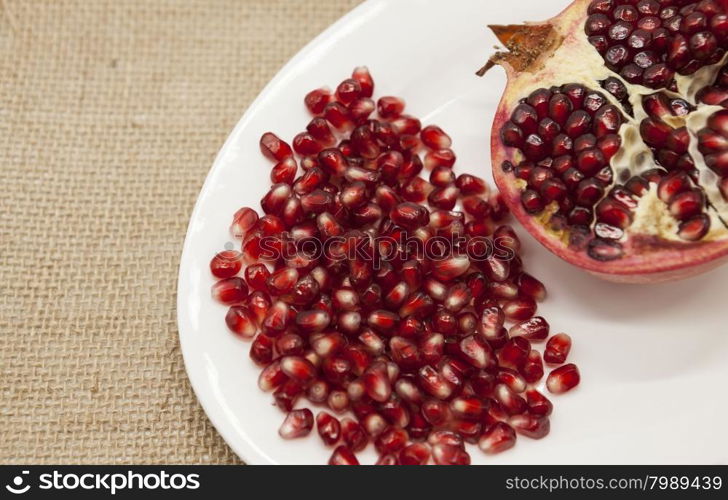 Pomegranates have broken into pieces with red berries on a porcelain plate on a textile background.. Pomegranates have broken into pieces with red berries on a porcelain plate on a textile background