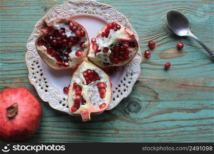 Pomegranates on white plate with spoon . Blue background .. Pomegranates on white plate with spoon . Blue background . .