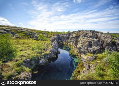 Pond surrounded by rocky cliffs in the wild nature of Iceland under a blue sky
