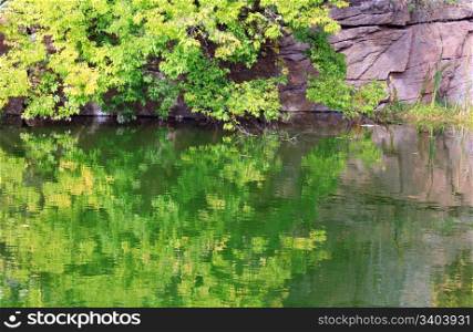 Pond water surface with reflection of colorful trees and rocky lakeside in autumn park