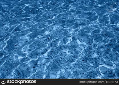 Pool water background. Ripples on blue transparent water in swimming pool with sun reflection. Top view. Trendy Banner with color of the year 2020