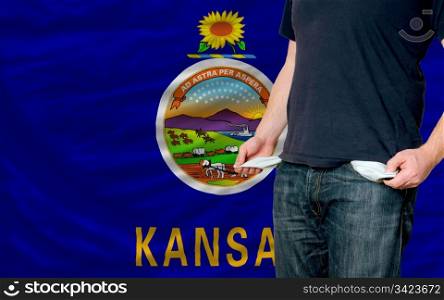poor man showing empty pockets in front of american state of kansas flag