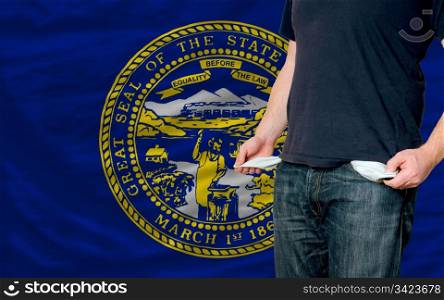 poor man showing empty pockets in front of american state of nebraska flag