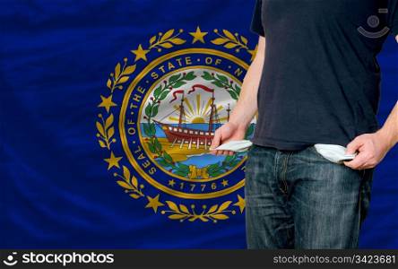 poor man showing empty pockets in front of american state of new hampshire flag