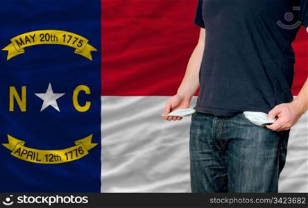 poor man showing empty pockets in front of american state of north carolina flag