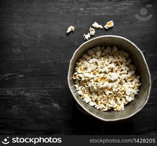 Popcorn in an old pot. On the black wooden table.. Popcorn in an old pot.