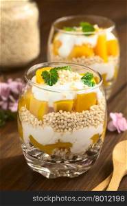 Popped quinoa, yogurt and peach parfait in glasses, photographed on dark wood with natural light (Selective Focus, Focus on the front of the leaves on the top)