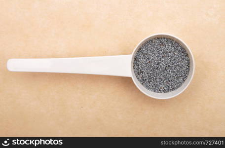 Poppy seeds in measuring spoon on brown background